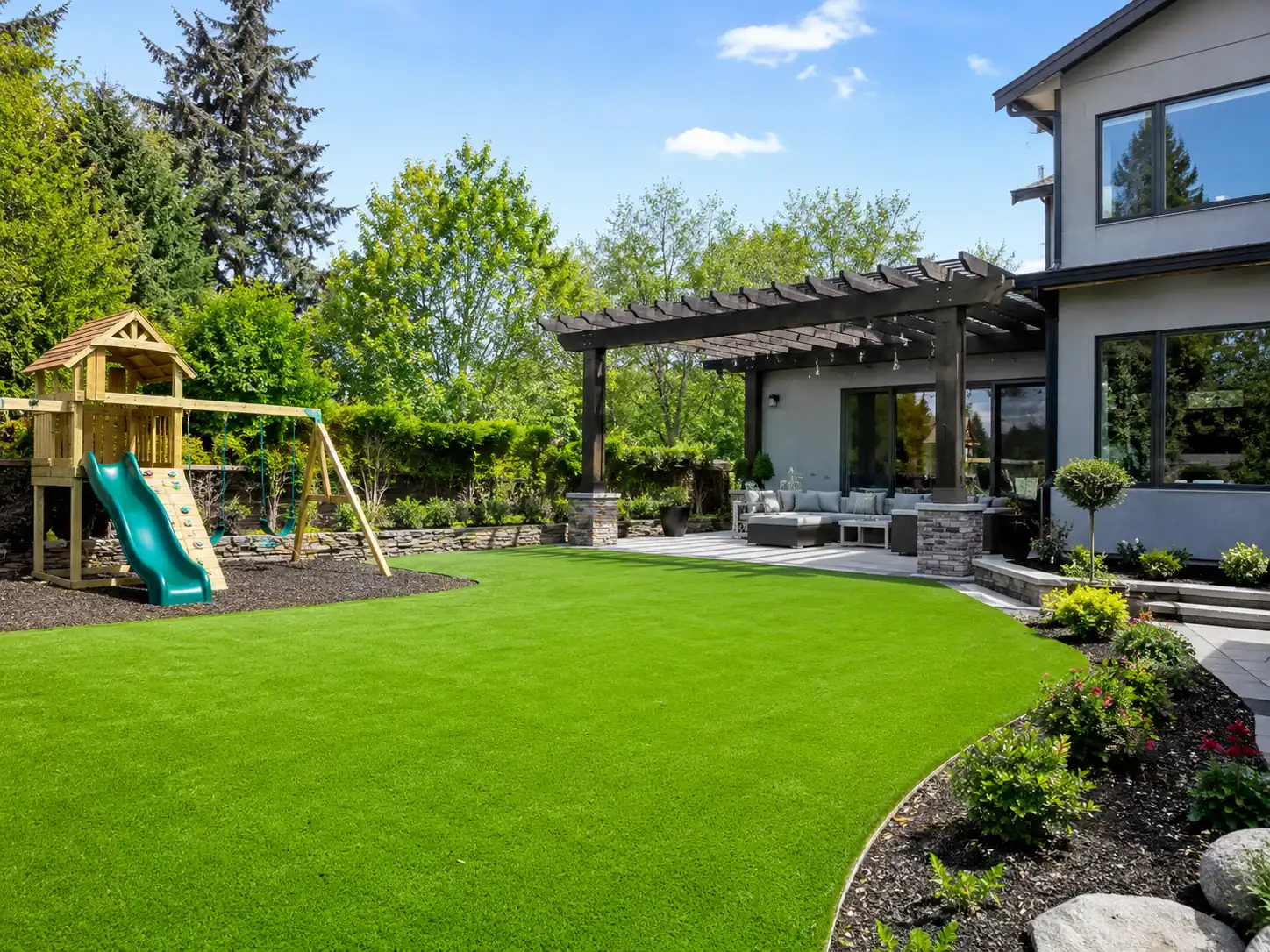 A vibrant commercial playground features bright equipment installed over soft temperature regulating artificial turf under a sunny sky.