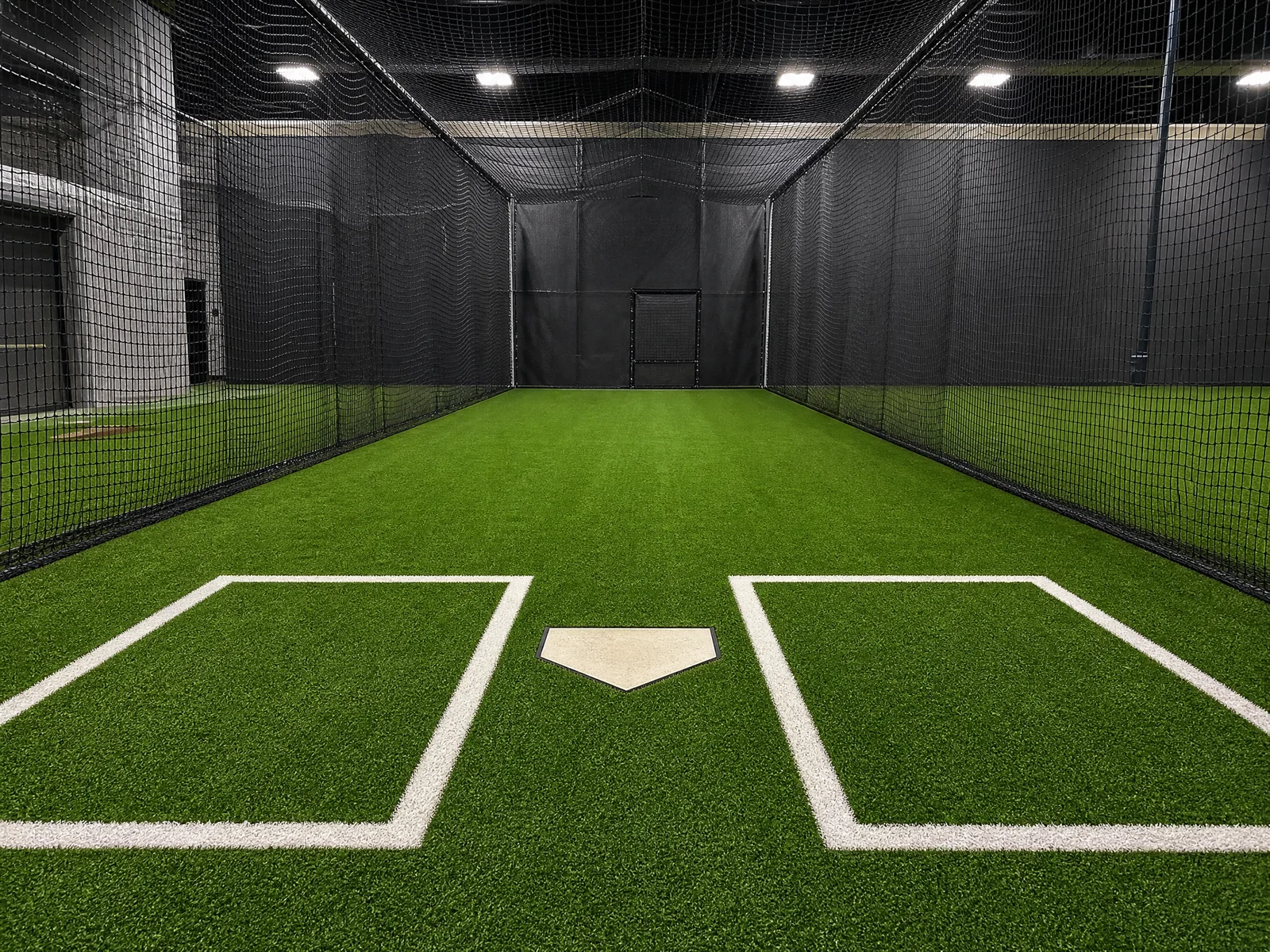 An indoor training facility featuring durable green sports turf laid out across a professional batting cage floor.