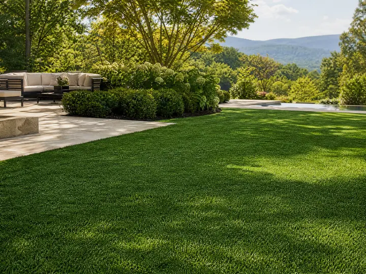 A vibrant green residential infilled landscape turf installation in a sunny backyard surrounded by garden landscaping and patio pavers.