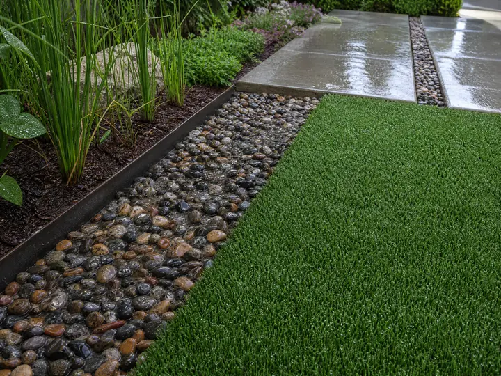 A lush green residential lawn featuring soft textured artificial turf installed across a sunny backyard patio area.