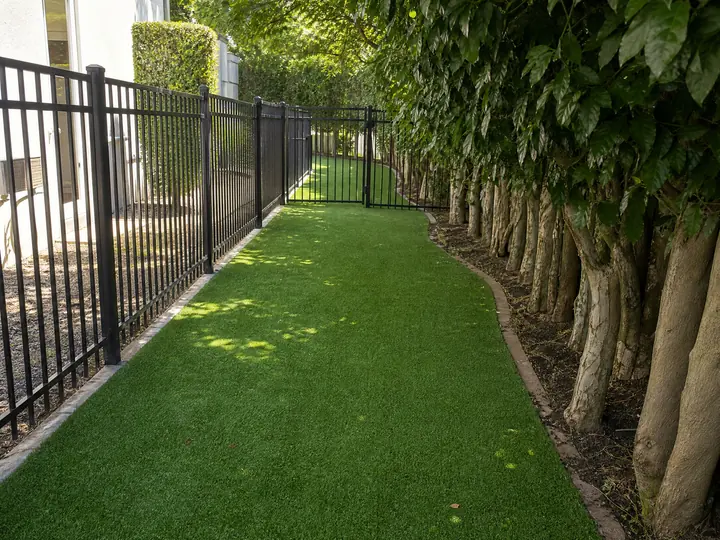 A vibrant green artificial turf installation designed for dogs playing in a spacious backyard dog run.
