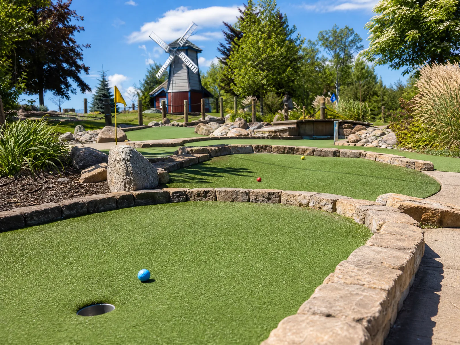 A lush backyard putting green featuring smooth green artificial turf surrounded by landscaping rocks and modern patio pavers.
