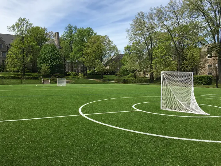A vibrant green lacrosse turf field marked with crisp white lines during an active training session under daylight.